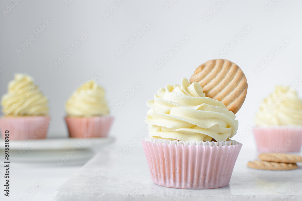 Pink cupcakes with tall american buttercream swirl and cookie garnish, cupcakes in pink liners with a tall vanilla buttercream and a cookie, birthday cupcakes on a white background Pink cupcakes with tall american buttercream swirl and cookie garnish, cupcakes in pink liners with a tall vanilla buttercream and a cookie, birthday cupcakes on a white background