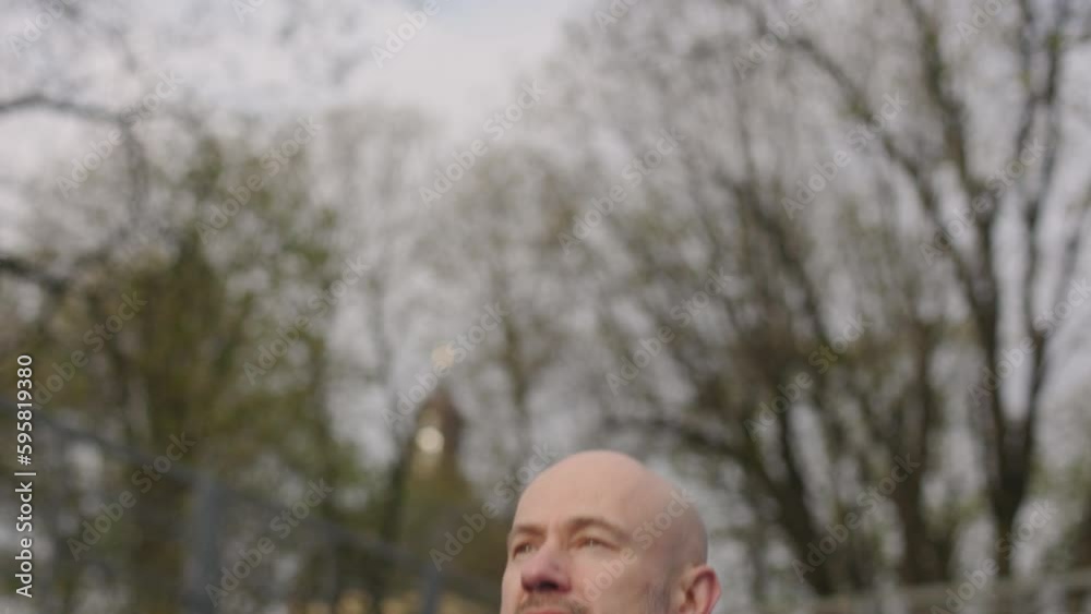 A bald man in a sportswear is exercising on a sports field. The amateur athlete is doing jumping jacks. Close up shot A bald man in a sportswear is exercising on a sports field. The amateur athlete is doing jumping jacks. Close up shot