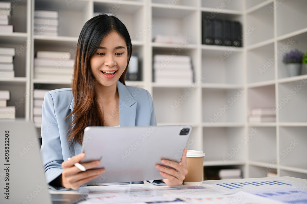 Charming Asian businesswoman using her digital tablet at her desk in the office.