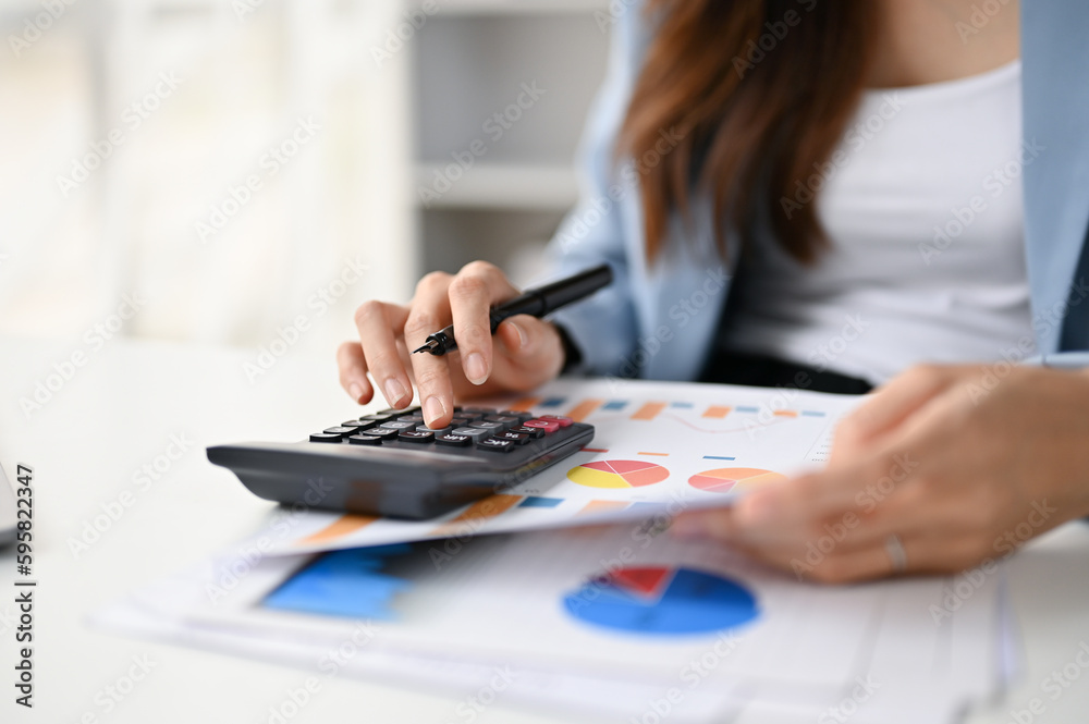 Close-up image of a female accountant using calculator and examining financial report