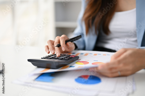 Close-up image of a female accountant using calculator and examining financial report
