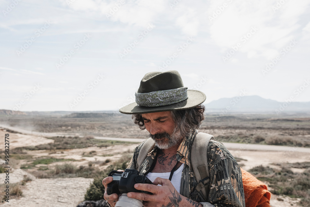 Traveler man with hat looking at the photos he takes from his camera in a desert