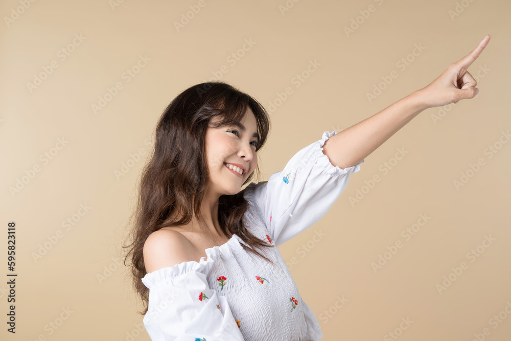 Young smiling Asian woman pointing finger sideways to copy space in brown color background. Young smiling Asian woman pointing finger sideways to copy space in brown color background.