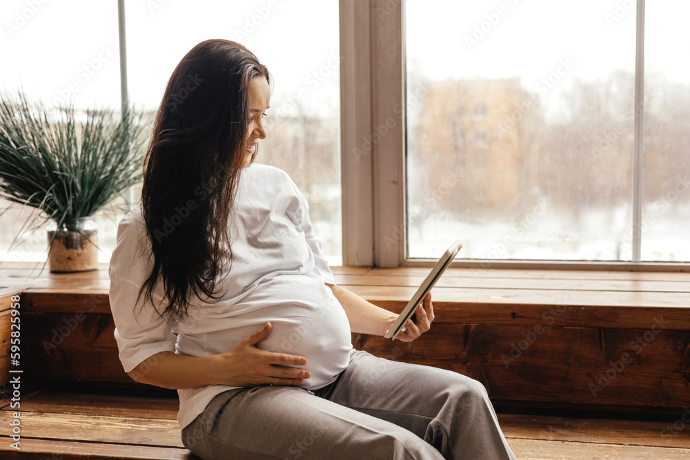 A pregnant cheerful girl communicates on a tablet. A pregnant cheerful girl communicates on a tablet.