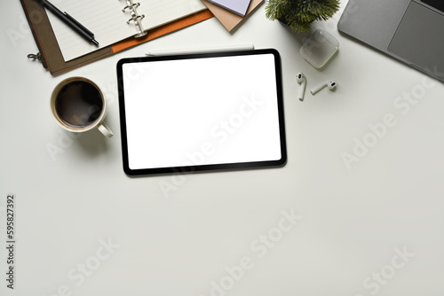 Digital tablet on white office desk table notebook, laptop and other office supplies. Top view with copy space.
