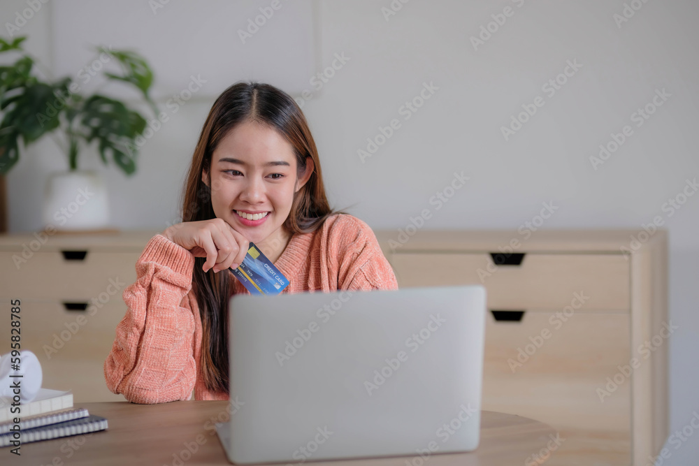 Young woman holding credit card and using laptop computer. Businesswoman working at home. Online shopping, e-commerce, internet banking, spending money, working from home concept