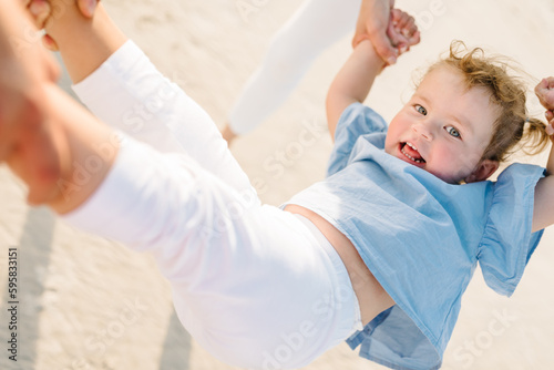 Happy family swings, throws up and spins his daughter outdoors. Mom, dad, and child relax on sand on a sandy beach together. Family day and childhood concept. Active funny games, lively play have fun.