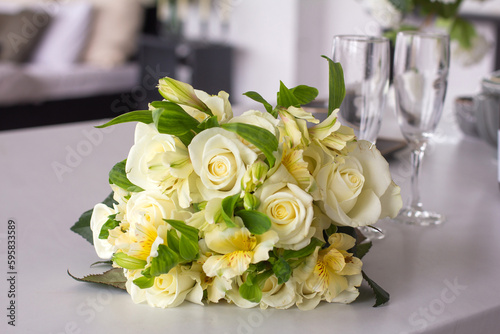 Festive delicate bouquet with light roses on the table against the background of glass glasses