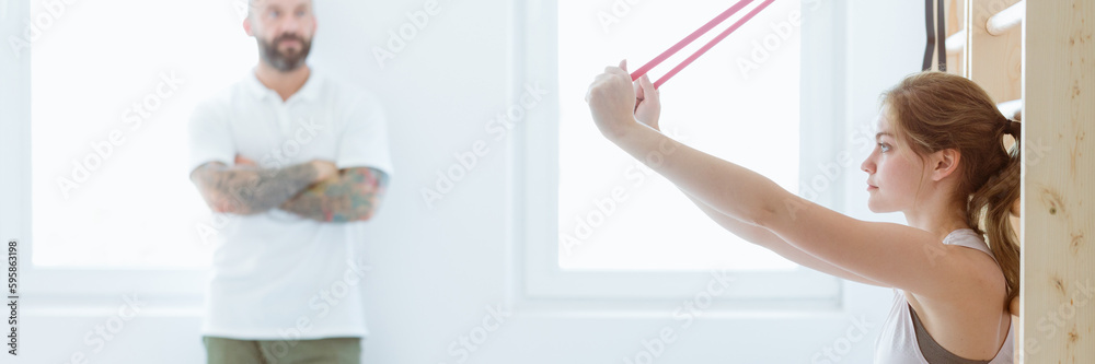 Young woman stretching her arms using tapes during a physiothera Young woman stretching her arms using tapes during a physiothera