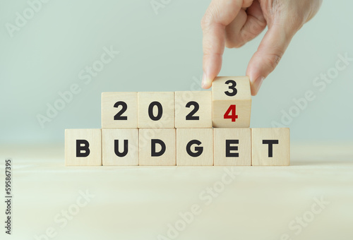 2024 Budget planning and allocation concept. Hand flips wooden cube and changes the inscription "BUDGET 2023" to "BUDGET 2024" with grey background, copy space. Use for banner and presentation.