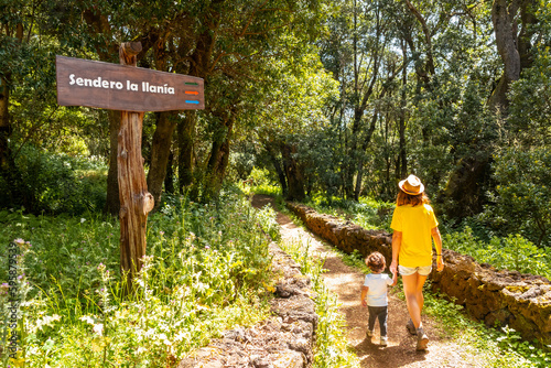 A mother with her son next to a sign identifying the La Llania trekking trail in El Hierro, Canary Islands. lush green landscape photo