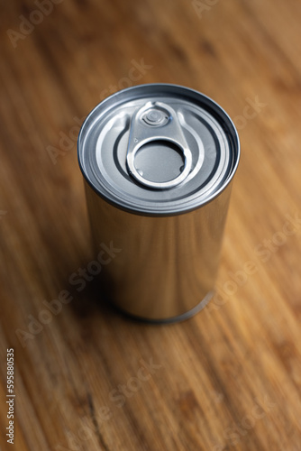 A blank, sealed tin metal food can on a wooden kitchen board. Close up shot, selective focus, no people
