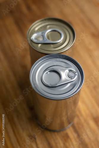 Two blank, sealed tin metal food cans on a wooden kitchen board. Close up shot, selective focus, no people