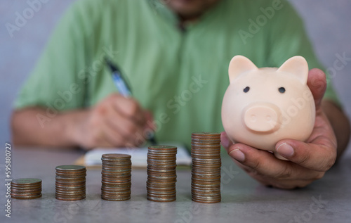 Man hand holding piggy bank and record account with step up the coin. Growing business to success and saving for retirement concept. Home accounting concept.