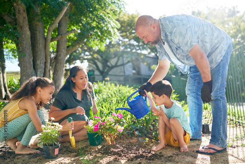 Family planting and watering flowers in sunny summer garden