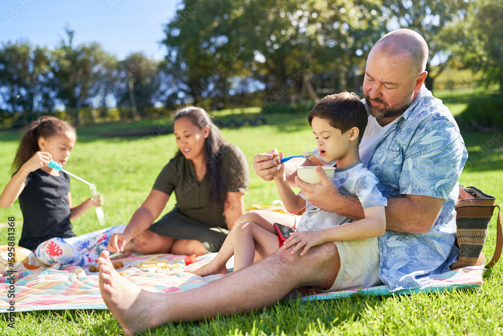 Father feeding cute son with Down Syndrome on picnic blanket Father feeding cute son with Down Syndrome on picnic blanket