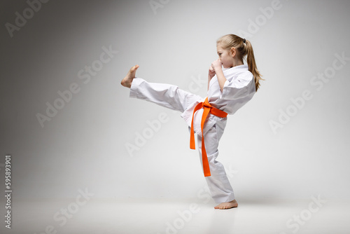 A child in a kimono kicks on a gray background, sports training.