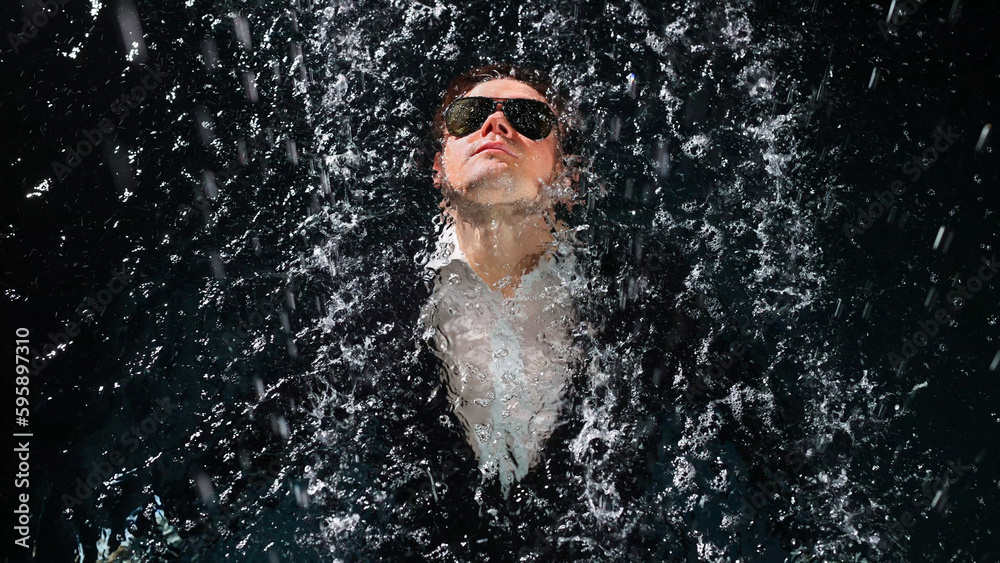 A man in a suit and sunglasses dives into the water in the rain. A man in a suit and sunglasses dives into the water in the rain.