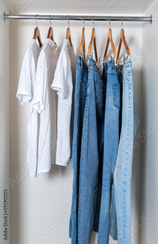 White T-shirts and blue jeans are neatly hung on hangers in a white closet.