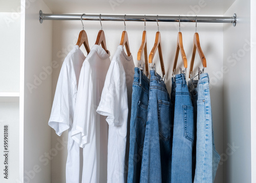 Close-up of white T-shirts and blue jeans hanging on a hangers in a white closet.