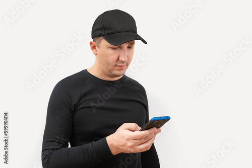 Young man in a baseball cap using a phone on a white background.