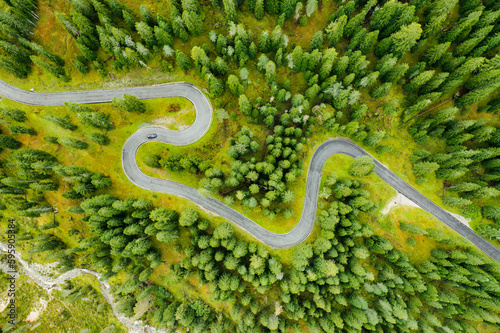 Driving cars on famous Snake Road on Italian Giau Pass. Driveway serpentine with cars surrounded by coniferous forests of Alpine mountains aerial view