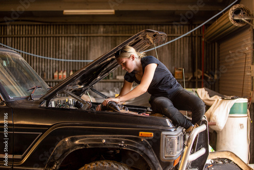 Female mechanic sitting on car hood leaning in repairing the car in workshop photo
