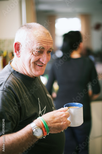 A Man in his 60s Standing Holding a Mug of White Tea, smiling. photo