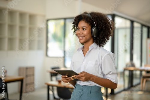 African american college student with headphones in hand with tablet standing smiling looking forward in cafe or workspace