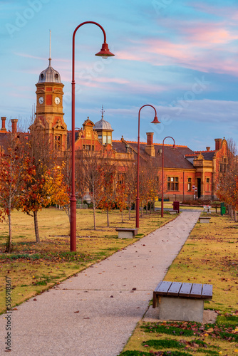 A path leading through apark to a  grand old railway station with a clock tower at twilight photo