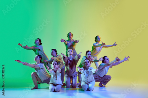 Fototapeta Naklejka Na Ścianę i Meble -  Group of young adorable girls moving to the beat of the music on gradient background in neon light. Teenage choreography studio