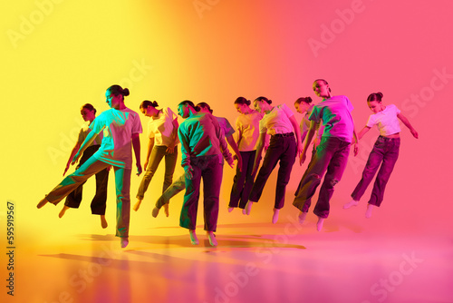 Fotografija Group of teenagers, young dancers standing in a row and jumping up on pink and yellow background in neon light