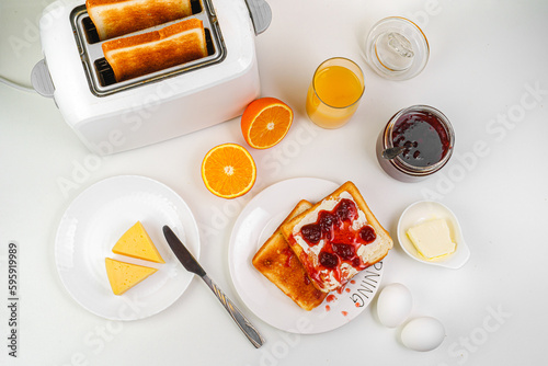 Healthy breakfast in the kitchen. Toaster and bread toast, freshly squeezed orange juice. Cheese, butter, lettuce. White toaster with healthy food and drinks on table in light kitchen
