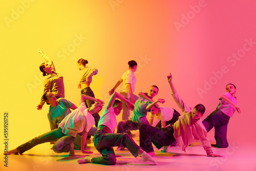 Group of teenagers, young dancers emotionally dancing together on pink and yellow gradient background in neon light. Girls dance club