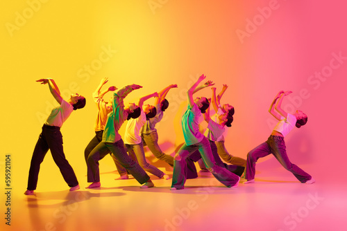 Group of beautiful teenage girls wearing white t-shirt and jeans dancing together on pink and yellow gradient background in neon light. Synchronicity