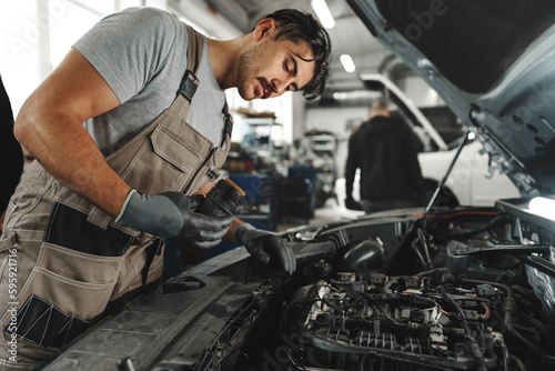 Young male mechanic examining engine under hood of car at the repair garage