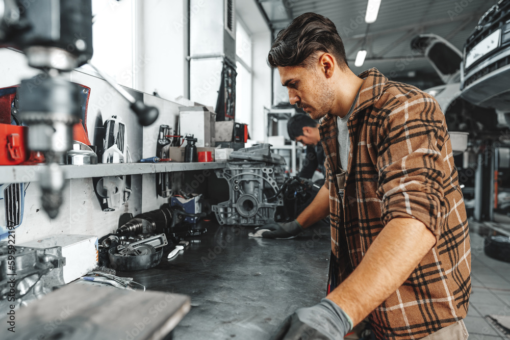Young man mechanic repairing car parts on worktable in car service shop Young man mechanic repairing car parts on worktable in car service shop