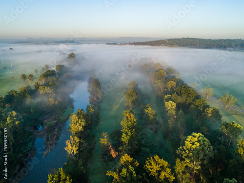 Mist drifting away over river at dawn in Hunter Valley leaving dew on riverside grass photo