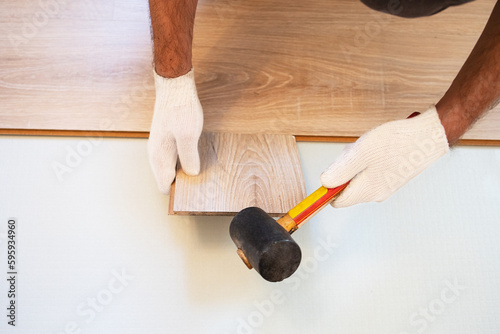 Top view mens hands in white gloves hammer laminate with a click clack system with a rubber mallet. Installing new laminate. Repairs. Carpenter, handyman, builder, mockup, copy space, reconstruction