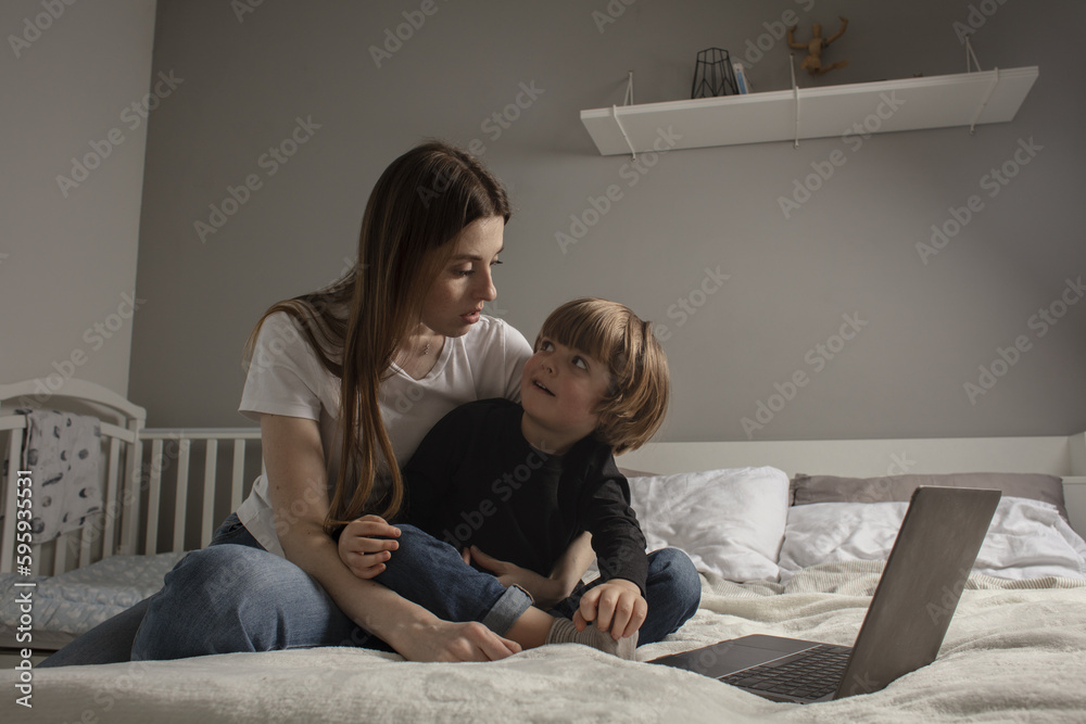 Happy mother with her little son enjoying in online shopping or working from home. Business from distance and virtual communication. Mom and baby watch cartoons or play game on laptop on the bed. Happy mother with her little son enjoying in online shopping or working from home. Business from distance and virtual communication. Mom and baby watch cartoons or play game on laptop on the bed.