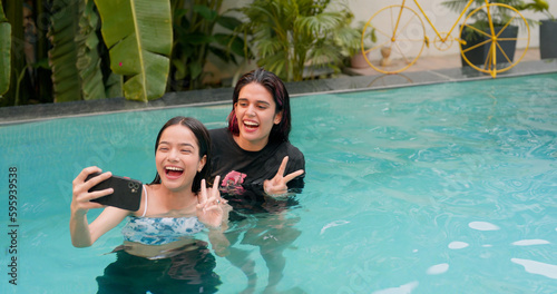 Smiling young women taking selfie in swimming pool female best friend using mobi Fototapet