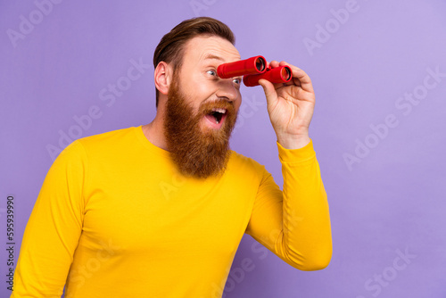 Photo of young red hair guy wear pullover hold binoculars watching explore empty space theater action isolated on violet color background