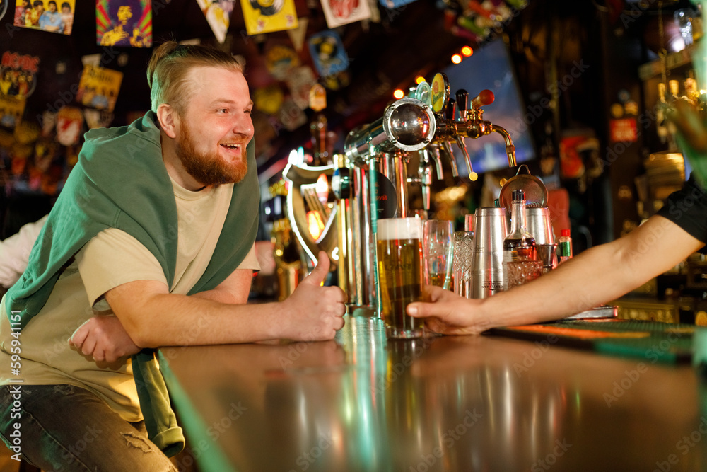 cheerful red-haired guy talking to the bartender and drinking beer