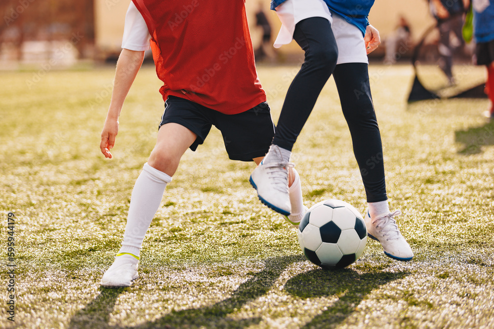 Obraz premium Red and Blue Soccer Players Compete in a Duel on Sunny Day. Football Game For Children. Soccer Background of Young Players Kicking Classic Soccer Ball
