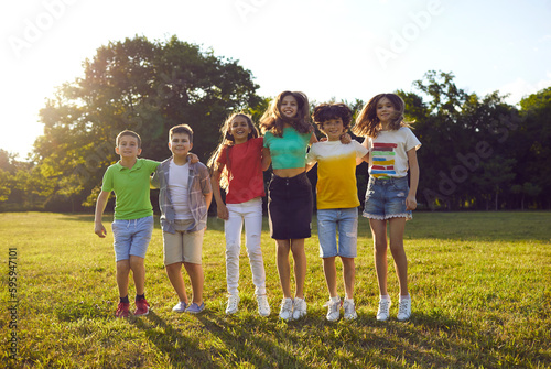 Happy children having fun on summer vacation. Bunch of school kids playing together and enjoying free time. Group of six overjoyed friends hugging and jumping on green park lawn in warm sunset light #595947101