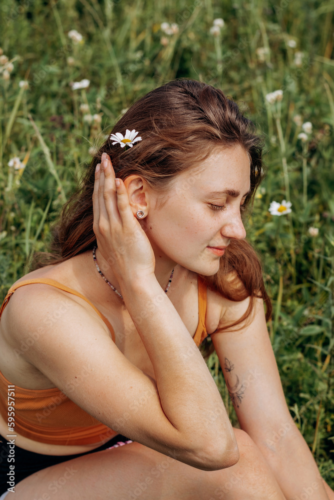Portrait of a happy young woman sitting in a meadow on a summer day with a daisy flower in her hair.Summer,happiness,natural beauty,slow life concept. Portrait of a happy young woman sitting in a meadow on a summer day with a daisy flower in her hair.Summer,happiness,natural beauty,slow life concept.