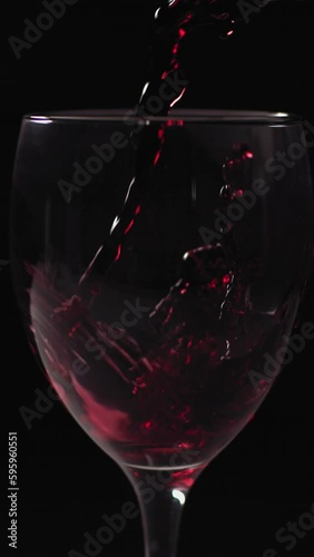 Red wine pouring from bottle into goblet. Close-up of red wine pouring in wine glass at black background. Slow motion. Macro shot with copy space