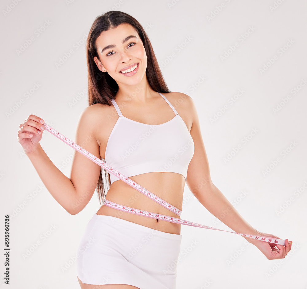 Pretty face, slim waist. Studio portrait of an attractive young woman using a measuring tape against a grey background. Pretty face, slim waist. Studio portrait of an attractive young woman using a measuring tape against a grey background.