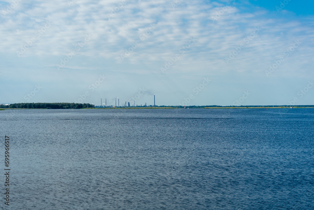 water surface, ripples on the water and clouds in the blue sky. industrial pipes with smoke