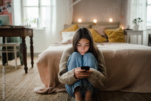 Fotografía Teenage girl sitting on the floor and scrolling her smartphone.